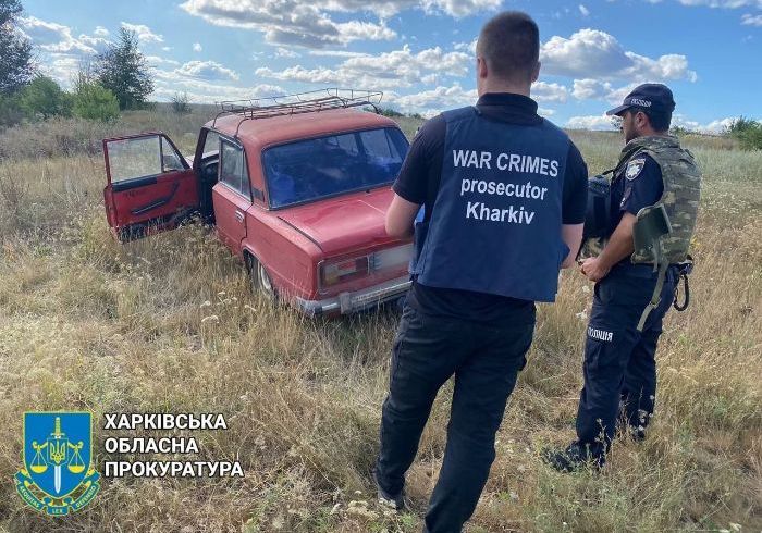 Двоє людей стоять біля автомобіля на галявині